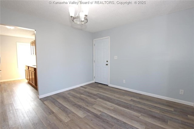 spare room featuring dark wood-type flooring, a chandelier, and a textured ceiling