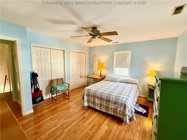 bedroom featuring ceiling fan, light hardwood / wood-style flooring, and multiple closets