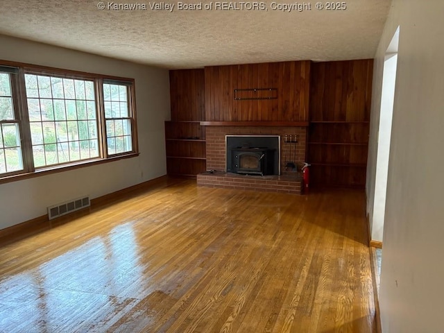 unfurnished living room featuring hardwood / wood-style flooring, wooden walls, a textured ceiling, and a wood stove