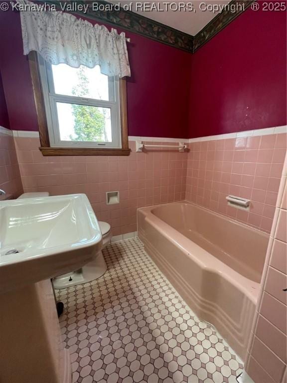 bathroom featuring toilet, a bathtub, and tile walls