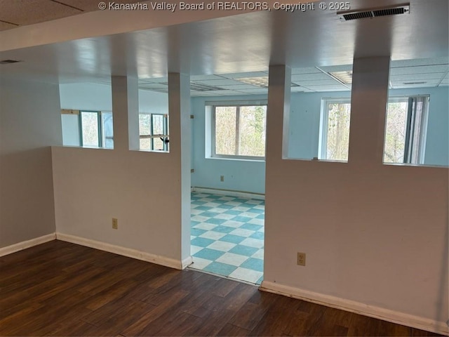 empty room featuring a drop ceiling, dark wood-type flooring, and a wealth of natural light