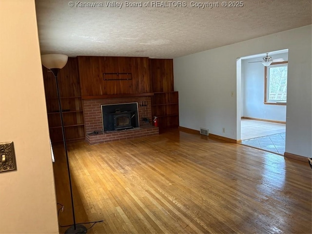 unfurnished living room featuring a wood stove, hardwood / wood-style floors, a textured ceiling, and wood walls