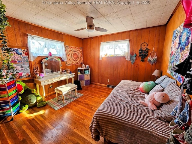 bedroom featuring ceiling fan, wooden walls, and hardwood / wood-style floors