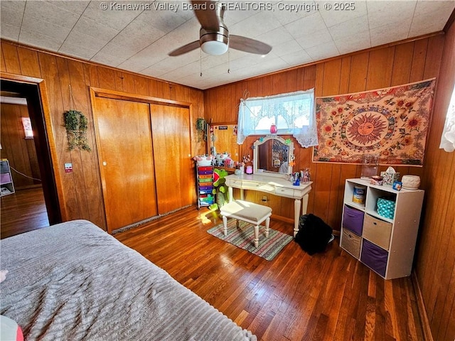 bedroom featuring ceiling fan, dark wood-type flooring, a closet, and wooden walls