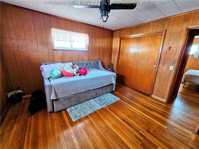 bedroom featuring hardwood / wood-style flooring, ceiling fan, and wood walls