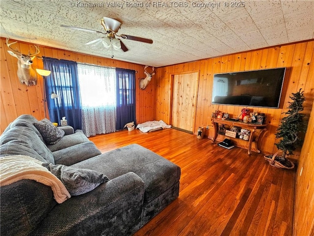 living room with hardwood / wood-style floors, ceiling fan, and wood walls