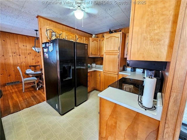 kitchen featuring ceiling fan, black fridge with ice dispenser, and wood walls