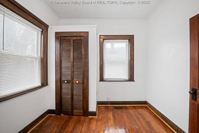 unfurnished bedroom featuring crown molding, multiple windows, dark hardwood / wood-style floors, and a closet