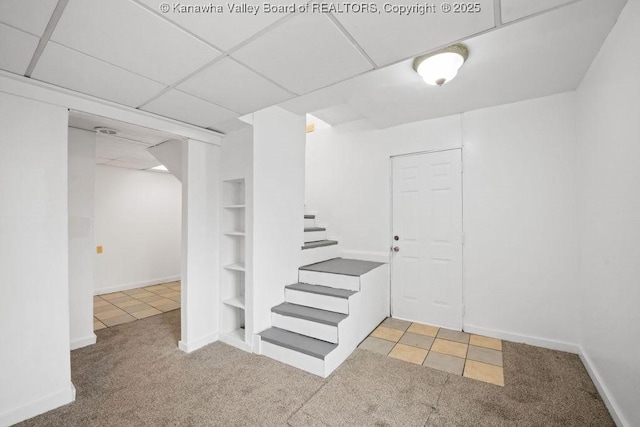 basement featuring light carpet, a paneled ceiling, and built in features