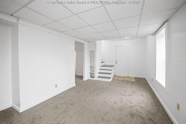 basement featuring carpet floors, a paneled ceiling, and built in features