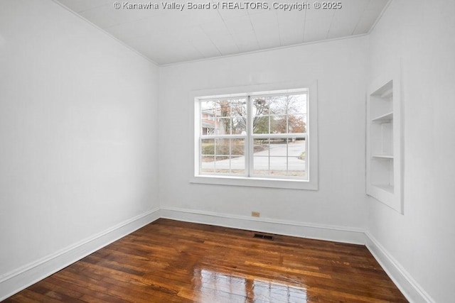 spare room featuring dark hardwood / wood-style flooring, crown molding, and built in features