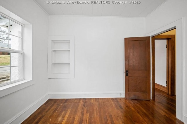 empty room with dark wood-type flooring, a wealth of natural light, and built in features