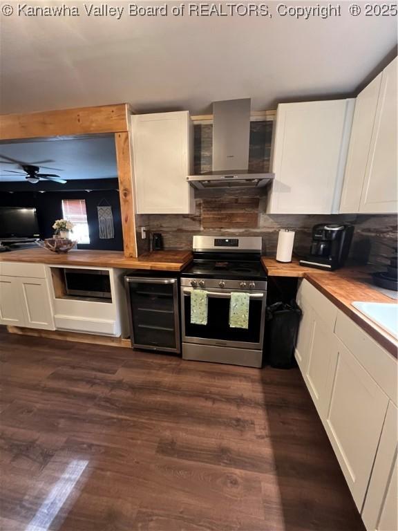 kitchen featuring stainless steel electric range, wooden counters, white cabinetry, beverage cooler, and wall chimney exhaust hood