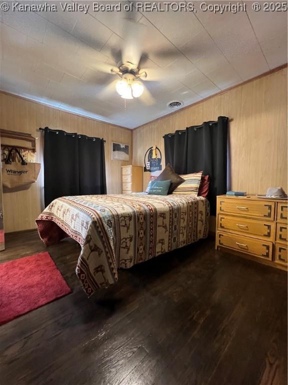 bedroom featuring crown molding, ceiling fan, dark hardwood / wood-style flooring, and wood walls