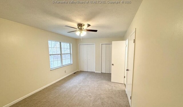 unfurnished bedroom featuring ceiling fan, a textured ceiling, light colored carpet, and multiple closets