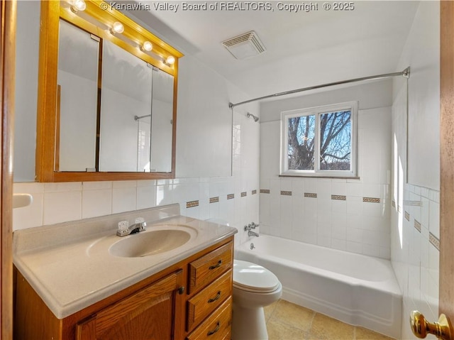 full bathroom with tile walls, tile patterned flooring, vanity, tiled shower / bath, and toilet