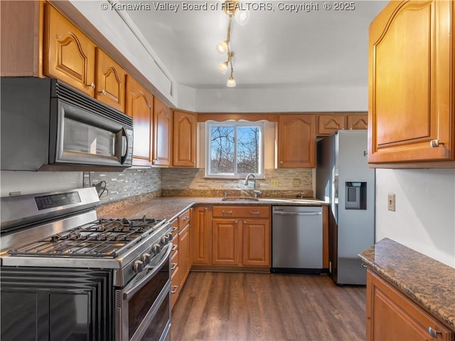 kitchen featuring sink, stainless steel appliances, dark hardwood / wood-style floors, tasteful backsplash, and dark stone counters