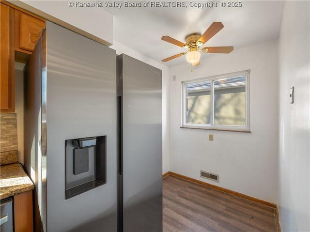 kitchen featuring stainless steel refrigerator with ice dispenser, light stone counters, dark hardwood / wood-style floors, ceiling fan, and decorative backsplash