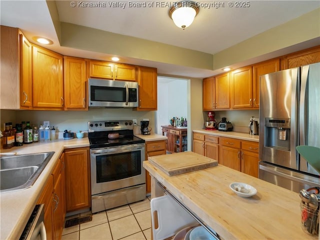 kitchen with wood counters, stainless steel appliances, sink, and light tile patterned floors