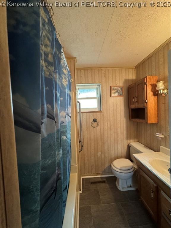 full bathroom with shower / tub combo with curtain, wooden walls, vanity, toilet, and a textured ceiling