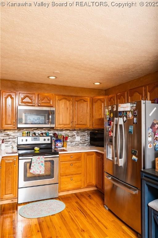 kitchen with decorative backsplash, light hardwood / wood-style flooring, stainless steel appliances, and a textured ceiling