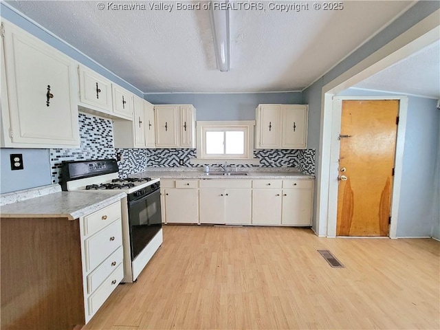 kitchen with sink, white cabinetry, range with gas stovetop, decorative backsplash, and light wood-type flooring