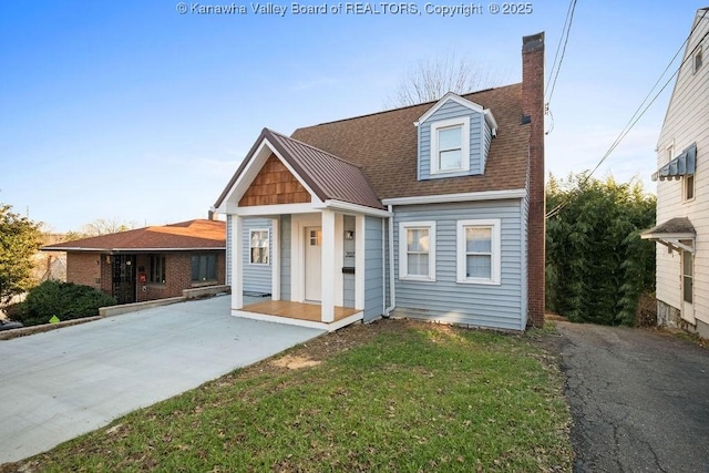 view of front of home with a front yard, roof with shingles, and a chimney