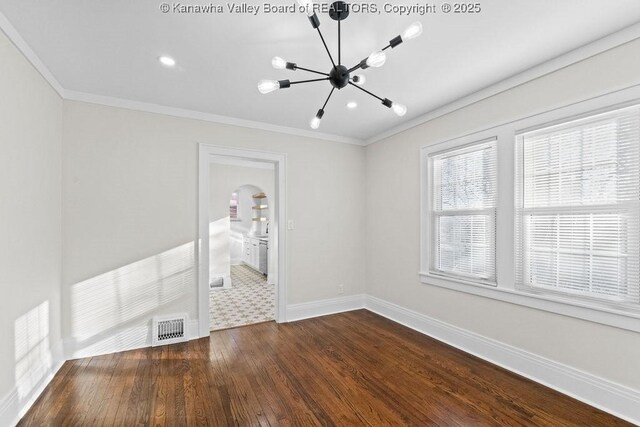 spare room featuring an inviting chandelier, crown molding, and dark wood-type flooring