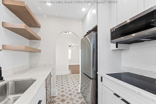 kitchen with sink, light stone counters, ornamental molding, stainless steel appliances, and white cabinets