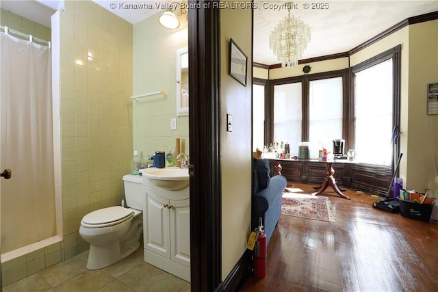 bathroom featuring tile walls, vanity, toilet, crown molding, and an inviting chandelier