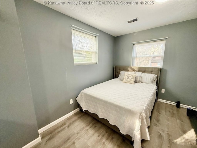 bedroom with multiple windows, a textured ceiling, and light hardwood / wood-style flooring