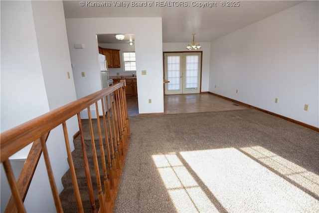 spare room featuring dark colored carpet, a notable chandelier, and french doors