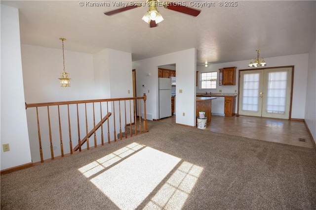 unfurnished living room featuring ceiling fan with notable chandelier, french doors, and carpet