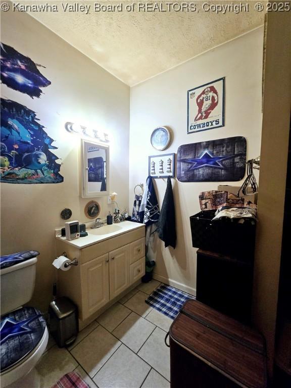 half bath with tile patterned floors, vanity, a textured ceiling, and toilet