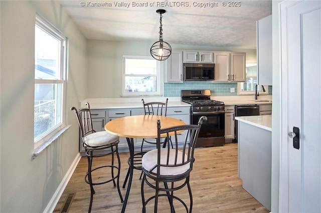 kitchen featuring decorative light fixtures, tasteful backsplash, gray cabinetry, stainless steel range with gas stovetop, and light hardwood / wood-style flooring