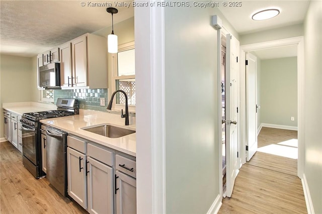 kitchen with light hardwood / wood-style floors, sink, stainless steel appliances, and hanging light fixtures