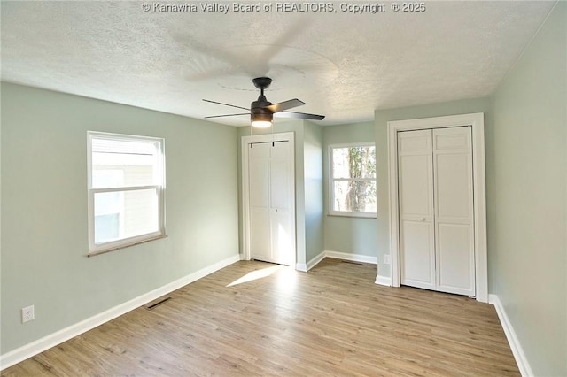 unfurnished bedroom featuring ceiling fan, light wood-type flooring, a textured ceiling, and two closets