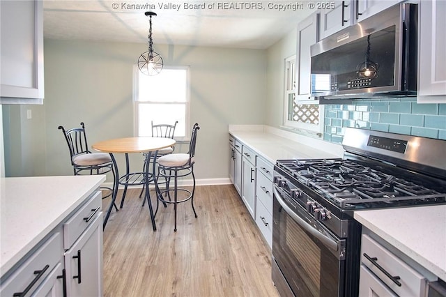 kitchen featuring stainless steel appliances, light hardwood / wood-style flooring, hanging light fixtures, and backsplash