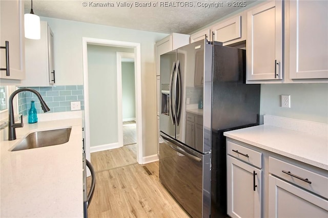 kitchen featuring sink, decorative light fixtures, stainless steel fridge with ice dispenser, light hardwood / wood-style floors, and decorative backsplash