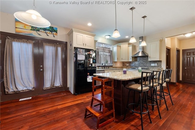 kitchen featuring pendant lighting, light stone counters, wall chimney exhaust hood, and black fridge