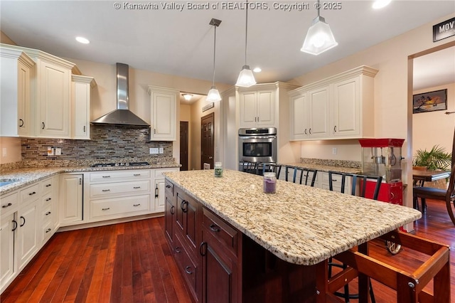 kitchen featuring pendant lighting, appliances with stainless steel finishes, wall chimney exhaust hood, and a breakfast bar area