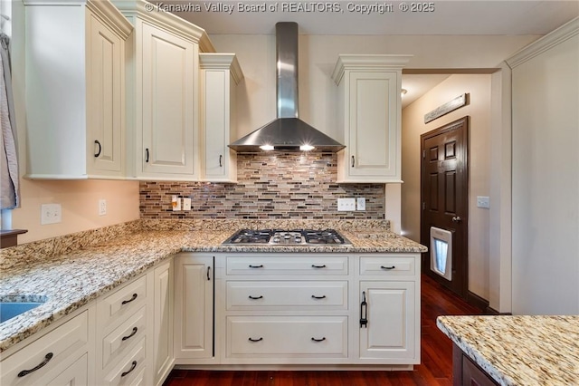 kitchen with light stone counters, backsplash, stainless steel gas cooktop, and wall chimney exhaust hood