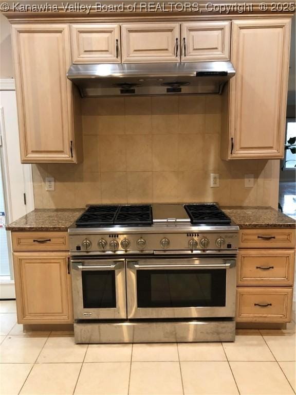 kitchen with dark stone countertops, double oven range, light tile patterned flooring, light brown cabinetry, and decorative backsplash