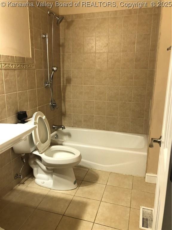 bathroom featuring toilet, tiled shower / bath combo, tile patterned flooring, and tile walls