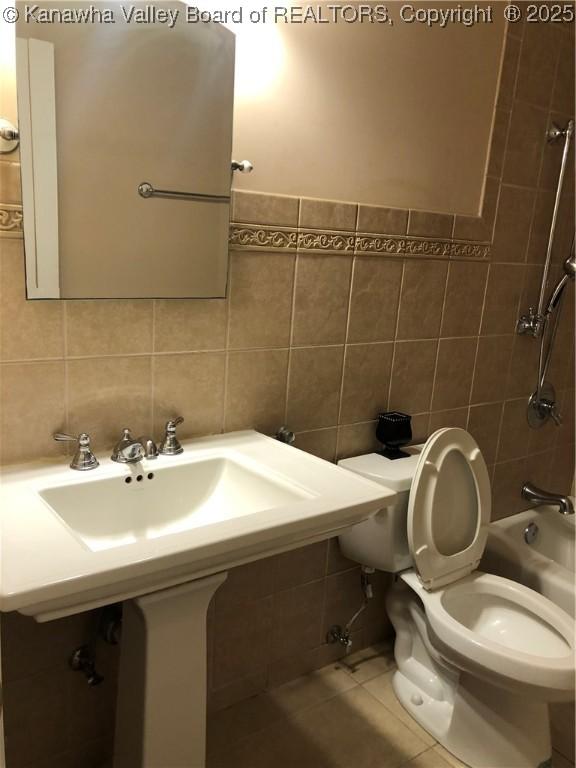 bathroom featuring tile patterned flooring, tile walls, washtub / shower combination, and toilet