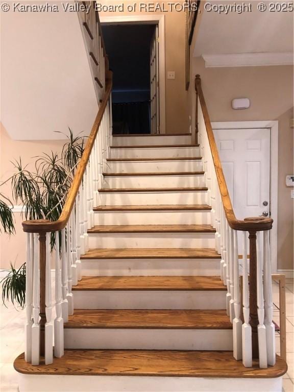 stairway with tile patterned floors and ornamental molding