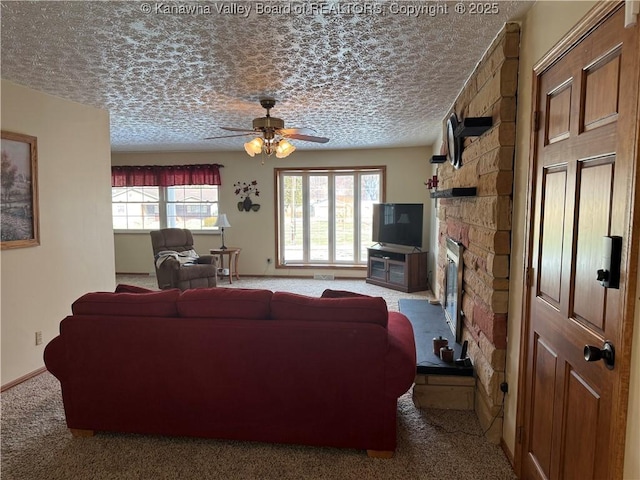 living room featuring ceiling fan, carpet flooring, a stone fireplace, and a textured ceiling