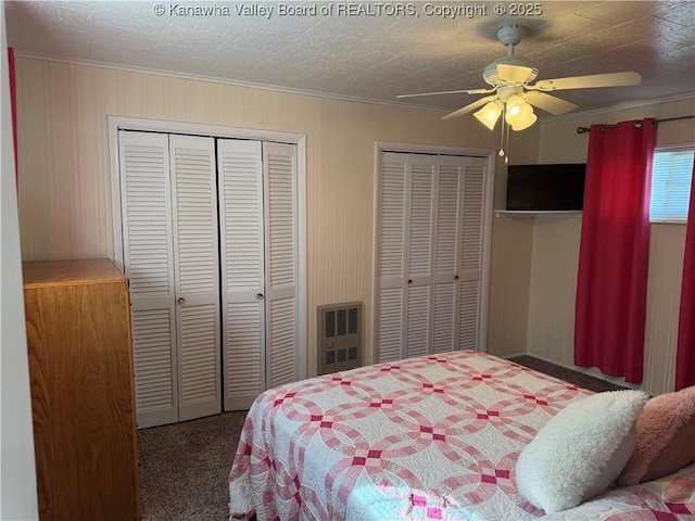 carpeted bedroom featuring ornamental molding, ceiling fan, and multiple closets