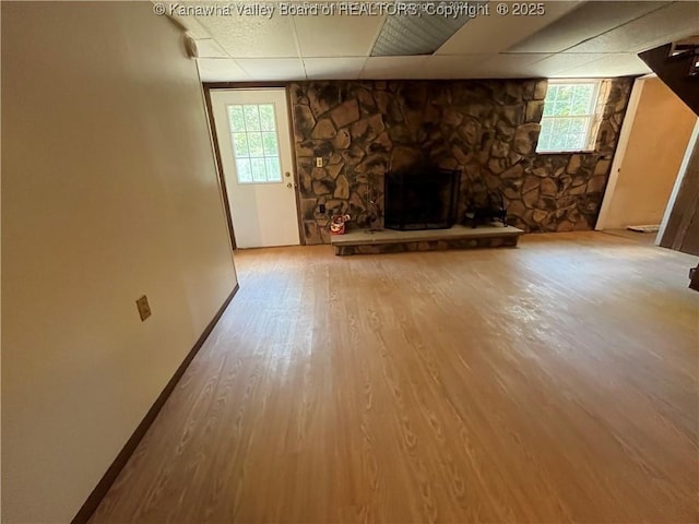 unfurnished living room featuring hardwood / wood-style floors, a drop ceiling, and a stone fireplace