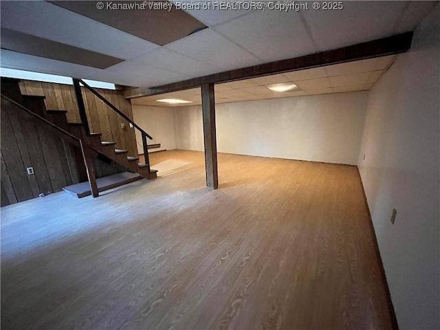 basement featuring hardwood / wood-style flooring, a paneled ceiling, wood walls, and baseboard heating